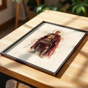 Puede incluir: Una impresi&oacute;n enmarcada que presenta una ilustraci&oacute;n en acuarela de una figura con armadura antigua, capa roja y un halo dorado. La figura sostiene una espada y se encuentra sobre un fondo claro. El marco es fino y negro, resaltando la obra.