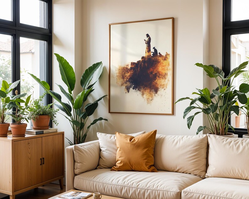May include: A framed wall art print featuring a silhouette of a standing figure and a kneeling figure on a rocky cliff edge, rendered in shades of brown, orange, and cream with a watercolour-style effect, displayed in a thin wooden frame.