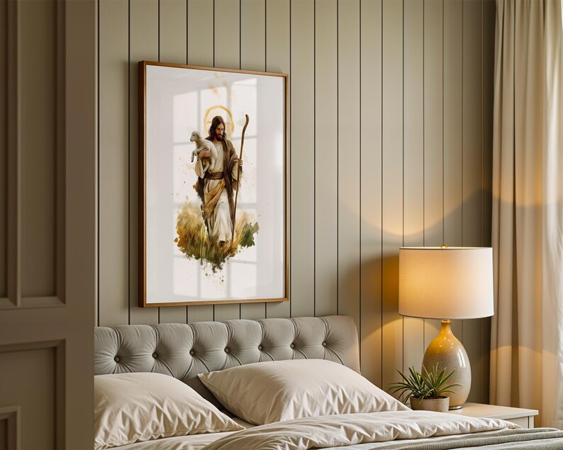May include: A framed wall art print featuring a watercolour-style illustration of a figure with long hair and a beard, wearing robes, holding a small lamb in one arm and a wooden staff in the other, set against a soft, abstract golden background.