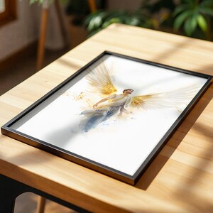 May include: A framed art print featuring a watercolor-style illustration of a figure with large, golden, feathered wings spread wide. The figure is depicted in a dynamic, ascending pose against a white background, with soft golden light accents.