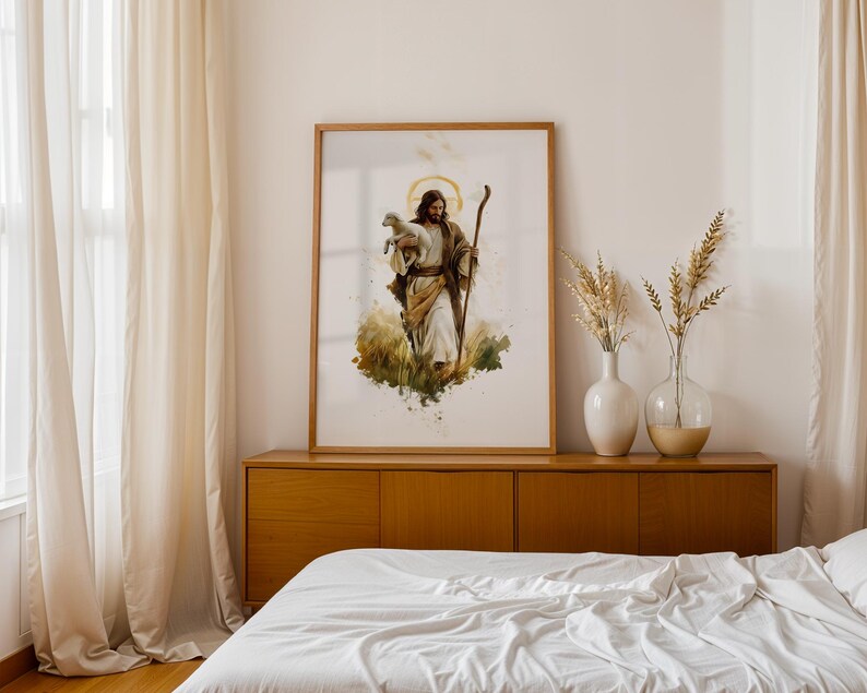 May include: A framed watercolour-style print depicting a figure with long hair and a beard, wearing robes and holding a small lamb in one arm while carrying a wooden staff in the other, set against a background of golden grass and a halo.