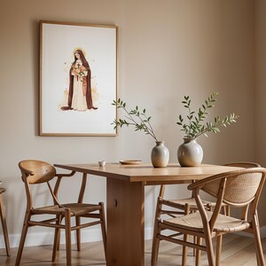 Peut inclure: Une impression d'art encadr&eacute;e repr&eacute;sentant une illustration &agrave; l'aquarelle d'une religieuse en habit marron tenant un bouquet de fleurs, expos&eacute;e dans une salle &agrave; manger avec une table en bois, quatre chaises &agrave; assise tress&eacute;e et deux vases en c&eacute;ramique.