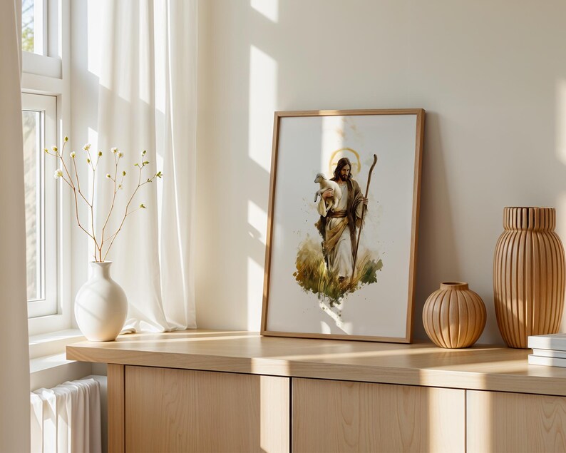 May include: A framed watercolour-style print depicting a figure with long hair and a beard, wearing robes and holding a small white lamb in one arm while carrying a wooden staff in the other hand, set against a soft, abstract golden halo background.
