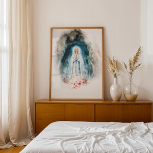 Puede incluir: Una l&aacute;mina de acuarela enmarcada que representa una figura con t&uacute;nica blanca y azul con las manos juntas en oraci&oacute;n, rodeada por un fondo de gruta azul oscuro y verde azulado con p&eacute;talos de rosa rojos esparcidos, en un marco de madera clara.