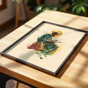 May include: A framed print featuring a watercolor-style illustration of a bearded figure in a green robe with a golden halo, seated while writing in a book. The artwork is set against a cream background and enclosed in a thin black frame.