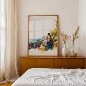 May include: A framed vertical wall art print featuring a watercolor-style illustration of a figure with long hair and robes sitting on a hillside, gesturing toward a large crowd gathered below near a body of water, with yellow and blue color tones.
