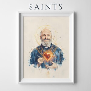 May include: A framed wall art print titled SAINTS featuring a watercolor-style portrait of a bearded person in a blue vestment with a glowing, fiery heart emblem on the chest and a golden halo, presented in a simple white rectangular frame.