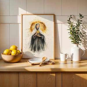 Pode incluir: Uma impress&atilde;o emoldurada em estilo aguarela que retrata uma figura com h&aacute;bito escuro e v&eacute;u branco a segurar um ostens&oacute;rio dourado, rodeada por um halo amarelo radiante. A obra est&aacute; exposta numa bancada de madeira junto a uma ta&ccedil;a de lim&otilde;es.