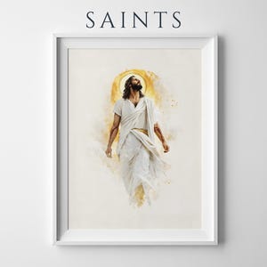 May include: A framed wall art print featuring the word SAINTS at the top. The artwork depicts a figure with long dark hair and a beard, wearing white robes, looking upward with a golden halo effect behind the head against a light background.
