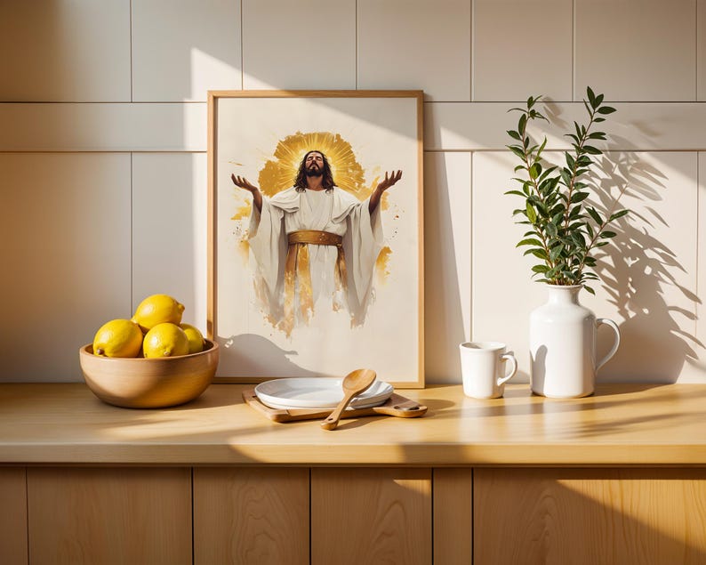 May include: A framed wall art print featuring a figure with long hair and a beard, wearing a white robe with a gold sash, arms raised, surrounded by a golden halo effect. The artwork is displayed in a light wood frame on a kitchen counter.