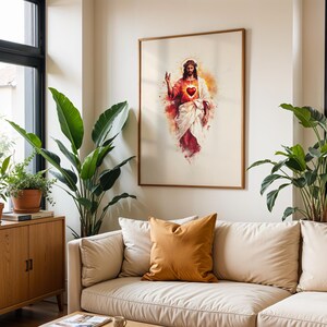 Puede incluir: Una l&aacute;mina de arte mural enmarcada que presenta una ilustraci&oacute;n estilo acuarela de Jesucristo con un Sagrado Coraz&oacute;n rojo brillante, vistiendo una t&uacute;nica blanca y una prenda roja, con un halo dorado, expuesta en una habitaci&oacute;n clara con plantas.