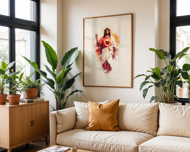 Puede incluir: Una l&aacute;mina de arte mural enmarcada que presenta una ilustraci&oacute;n estilo acuarela de Jesucristo con un Sagrado Coraz&oacute;n rojo brillante, vistiendo una t&uacute;nica blanca y una prenda roja, con un halo dorado, expuesta en una habitaci&oacute;n clara con plantas.
