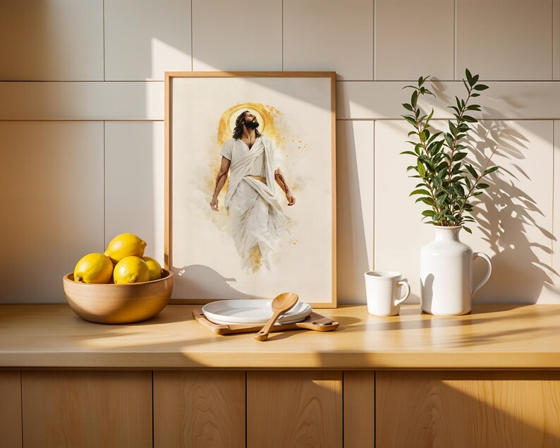 May include: A framed wall art print depicting a figure in white robes with a golden halo, positioned above a wooden counter with a bowl of yellow lemons, a white plate, a wooden spoon, a white mug, and a white vase containing green foliage.