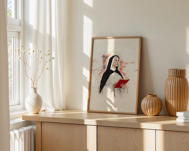 May include: A framed wall art print featuring a portrait of a nun wearing a black and white habit, holding an open red book. Behind the figure is a stylized red and orange watercolor-style burst. The artwork is presented in a light wood frame.