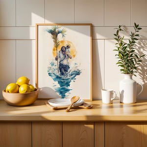 May include: A framed watercolor-style print depicting a figure carrying a child on their shoulders while walking through blue water, holding a palm frond. The artwork features a yellow sun halo and is displayed in a light wood frame on a counter.