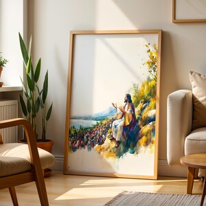 May include: A framed vertical wall art print featuring a watercolour-style illustration of a figure with long hair and a robe sitting on a hillside, gesturing towards a large crowd gathered below near a body of water, with yellow and blue tones.