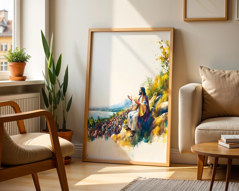 May include: A framed vertical wall art print featuring a watercolour-style illustration of a figure with long hair and a robe sitting on a hillside, gesturing towards a large crowd gathered below near a body of water, with yellow and blue tones.