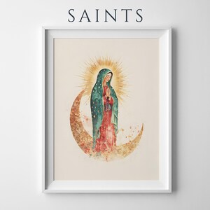 May include: A framed art print featuring the word SAINTS at the top. The illustration depicts a figure in a teal cloak with gold stars and a red dress, standing on a crescent moon with a golden sunburst halo behind the head, all on a cream background.