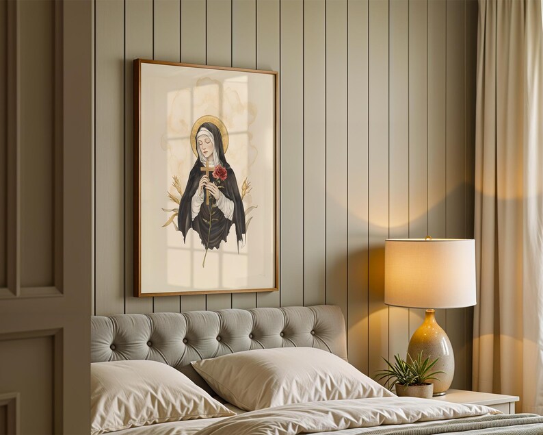 Op de afbeelding: Een ingelijste muurkunstprint met een gestileerde illustratie van een figuur in een zwart habijt en witte sluier, die een houten kruis en een rode roos vasthoudt. De figuur heeft een gouden halo tegen een lichte cr&egrave;mekleurige achtergrond.