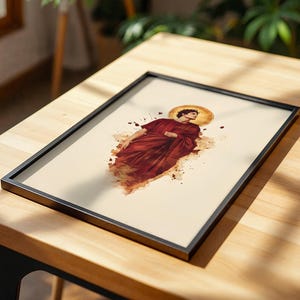 May include: A framed art print featuring a watercolour-style illustration of a figure in a deep red robe with a golden halo. The artwork is set against a cream-coloured background, enclosed in a thin black frame, showcasing a blend of classical and abstract artistic elements.