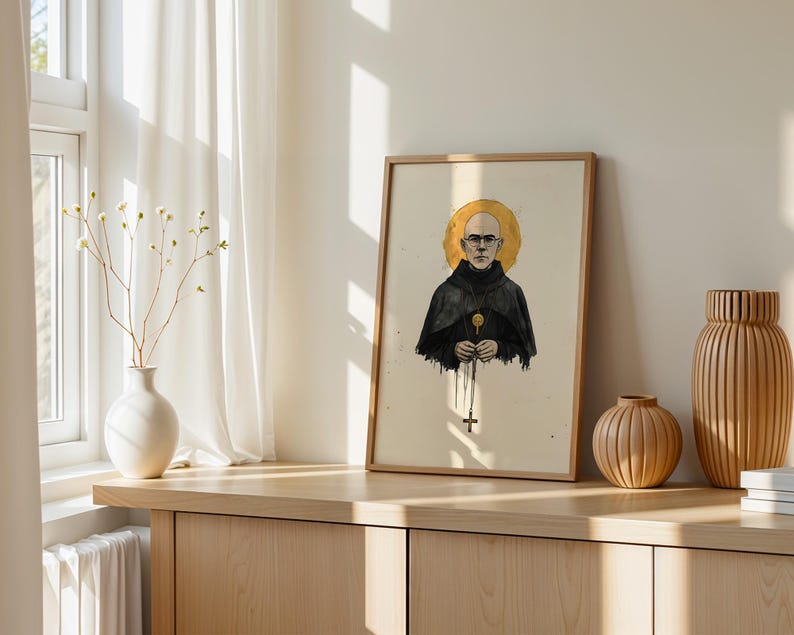 May include: A framed art print featuring a digital illustration of a bald person wearing glasses and a dark hooded robe. The figure has a golden circular halo behind their head and holds a rosary with a cross pendant against a cream background.