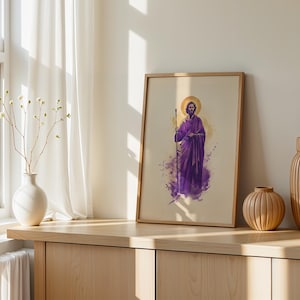 May include: A framed vertical print featuring a watercolor-style illustration of a bearded figure in a purple robe holding a staff, with a golden halo behind the head, set against a light beige background with purple and yellow paint splashes.