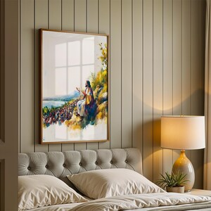 May include: A framed vertical wall art print featuring a watercolour-style illustration of a figure in robes sitting on a hillside, gesturing towards a large crowd gathered below near a body of water, with yellow and green foliage accents.