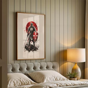 May include: A framed wall art print featuring a knight in full armour standing over a dark creature. The knight holds a sword and a shield with a red cross. A large red circle serves as a backdrop with black ink splatter effects on a white background.