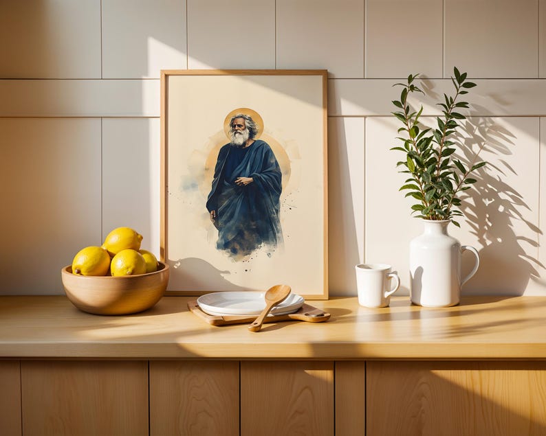 May include: A framed art print featuring a watercolor illustration of a bearded figure in a dark blue robe with a golden halo. The print is displayed alongside a wooden bowl of yellow lemons, a white plate with a wooden spoon, and a white vase.