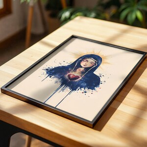 May include: A framed art print featuring a watercolor-style illustration of a figure with closed eyes wearing a dark blue hooded cloak. A glowing red heart is centered on the chest, surrounded by golden light rays against a cream background.