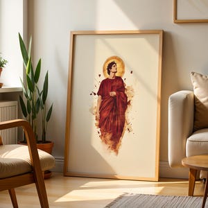 May include: A framed vertical wall art print featuring a central figure dressed in a deep red robe with a golden halo behind the head. The illustration uses a watercolour style with abstract splashes of red and brown ink surrounding the figure.