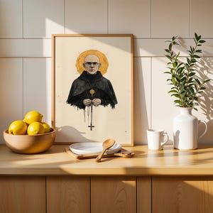 May include: A framed art print featuring a bald person wearing glasses and a black hooded robe with a gold halo behind their head. The figure holds a rosary with a cross pendant. The illustration is set against a light cream background.