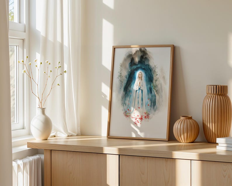 Puede incluir: Una l&aacute;mina de acuarela enmarcada que representa una figura con t&uacute;nica blanca y azul con las manos juntas en oraci&oacute;n, rodeada por un fondo abstracto azul oscuro y gris con detalles florales rojos en la base, en un marco de madera clara.