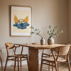 May include: A framed wall art print featuring two cherubs with golden wings resting on a dark blue cloud with small yellow stars, set against a light cream background. The artwork is displayed in a simple wooden frame on a plain wall.