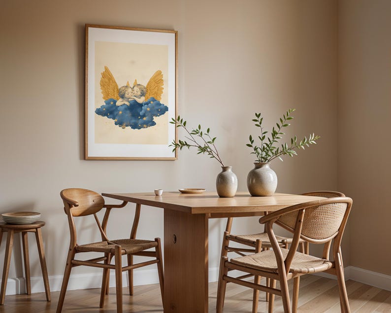 May include: A framed wall art print featuring two cherubs with golden wings resting on a dark blue cloud with small yellow stars, set against a light cream background. The artwork is displayed in a simple wooden frame on a plain wall.
