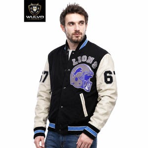 Puede incluir: Una chaqueta universitaria negra con mangas color crema, que presenta el texto LIONS y un gráfico de un casco de fútbol americano en el pecho. El número 67 aparece en ambas mangas. La chaqueta tiene cierre de botones y ribetes a rayas azul y negro.