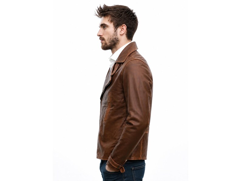 May include: A brown leather jacket with a classic collar, long sleeves, and a buttoned cuff detail. The jacket is worn over a white collared shirt and dark blue denim jeans, showcasing a smooth texture and a structured fit for the upper body.