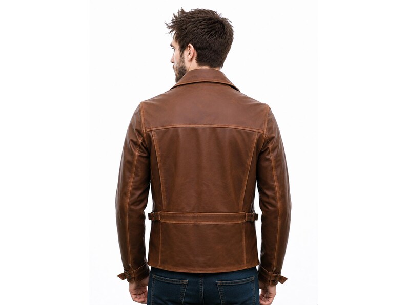 May include: A brown leather jacket featuring a wide collar, long sleeves with adjustable cuffs, and a horizontal back belt detail with side buckles. The jacket has visible seam stitching and a structured fit, worn over dark blue denim jeans.