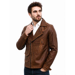May include: A brown leather jacket featuring a wide notched collar, an asymmetrical front zipper closure, and two front pockets with flaps. The jacket includes long sleeves with adjustable buckled straps at the cuffs and a white collared shirt underneath.