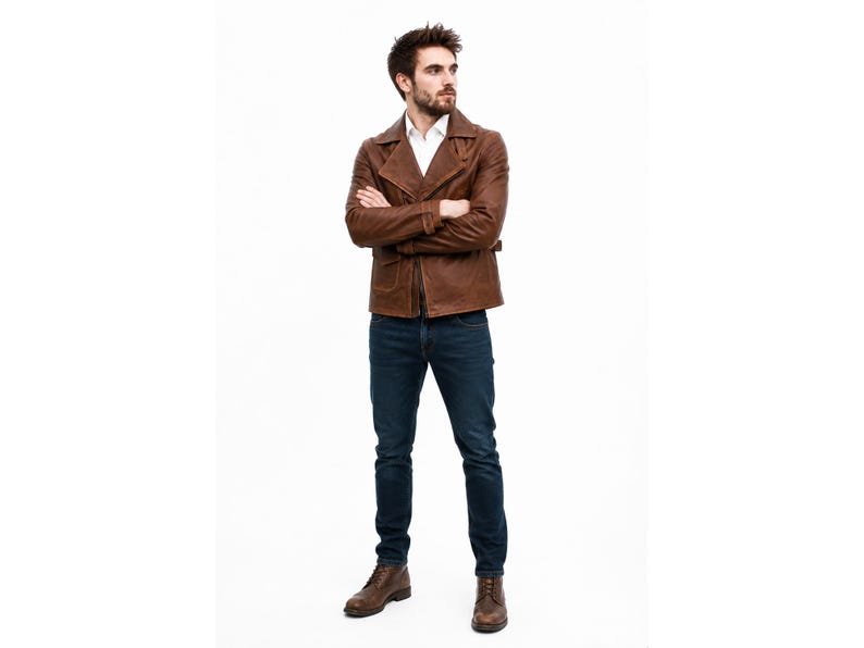 May include: A brown leather jacket with a wide collar and front zipper, worn over a white collared shirt. The outfit includes dark blue denim jeans and brown leather lace-up boots. The jacket features long sleeves and a structured fit.