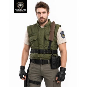 May include: An olive green tactical vest featuring a high collar, two front chest pockets, and a brown shoulder strap. The vest is worn over a beige short-sleeved shirt, paired with a black utility belt, black fingerless gloves, and grey cargo pants.