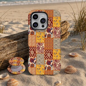 Könnte beinhalten: Eine Smartphone-Hülle und ein passender runder, zusammenklappbarer Handyhalter mit einem lebendigen Patchwork-Design, das sich wiederholende Blumen-, geometrische und Paisley-Muster in Senfgelb, Dunkelrot, Weiß und Dunkelblau zeigt.