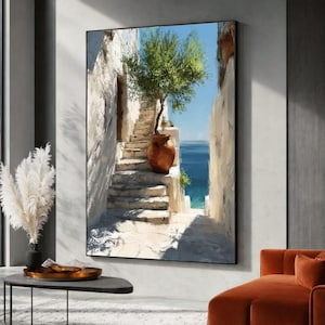 May include: A framed wall art print depicting a Mediterranean scene with stone stairs leading toward a blue sea. A terracotta pot containing a green tree sits on the steps between white stone walls under a bright blue sky with clear sunlight.