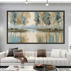 May include: A framed landscape painting depicting a serene waterscape with trees. The artwork features a palette of blues, golds, and browns, with the trees reflected in the water. The painting is displayed above a white sofa in a modern living room setting.