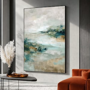 May include: Abstract landscape painting in a black frame. The artwork features a blend of teal, beige, and white hues, creating a serene and naturalistic scene. The painting is displayed on a neutral-colored wall.