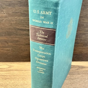 May include: A vintage book with a teal cover and gold lettering. The title reads "U.S. ARMY IN WORLD WAR II." The spine features text about technical services and transportation corps operations. The book is slightly worn, suggesting age.