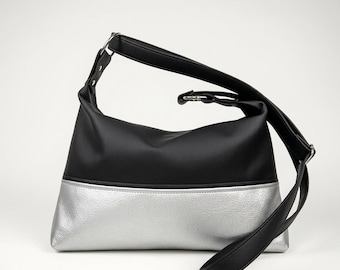 May include: A black and silver shoulder bag with a long adjustable strap. The top half of the bag is black, and the bottom half is silver. The bag has a simple, modern design.