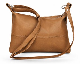 May include: A tan shoulder bag with a smooth, matte finish. The bag features a horizontal seam across the lower section, a top zipper closure, and a long, adjustable strap attached to the sides with silver-toned metal rings and rivets.