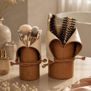 Peut inclure: Deux contenants de rangement cylindriques en matériau beige avec des rabats intérieurs crème et des fermetures à cordon. Le plus petit contient divers pinceaux de maquillage, tandis que le plus grand contient une brosse et un peigne.