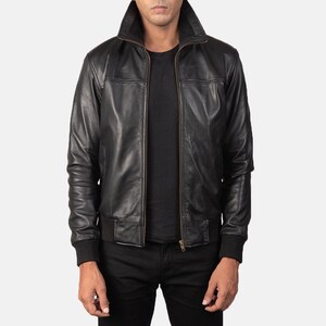 Könnte beinhalten: Eine schwarze Lederjacke mit hohem Kragen, durchgehendem Frontreißverschluss sowie gerippten Strickbündchen an Ärmeln und Saum. Die Jacke hat eine glatte Oberfläche, lange Ärmel und eine strukturierte Passform, getragen über einem schwarzen Shirt.
